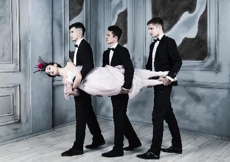Dreieinigkeit. Drei Männer im Smoking tragen eine Ballerina im Arm