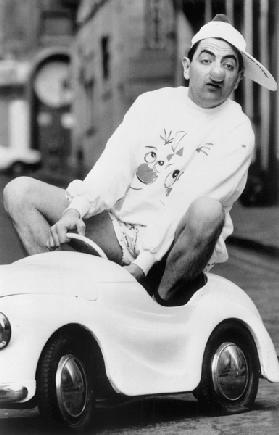 Le comedien britannique Rowan Atkinson portant un nez de clown dans une voiture pour enfant 1989