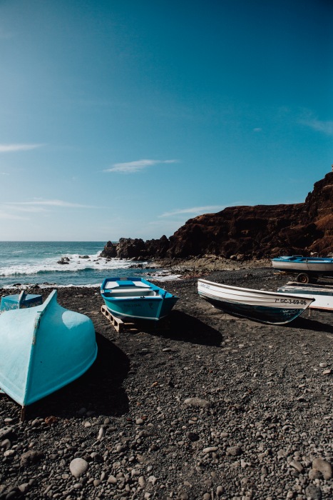 Blaue Boote auf schwarzem Vulkansstrand auf Lanzarote von Laura Nenz