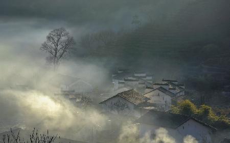 Das Dorf mit aufsteigendem Rauch im Morgennebel